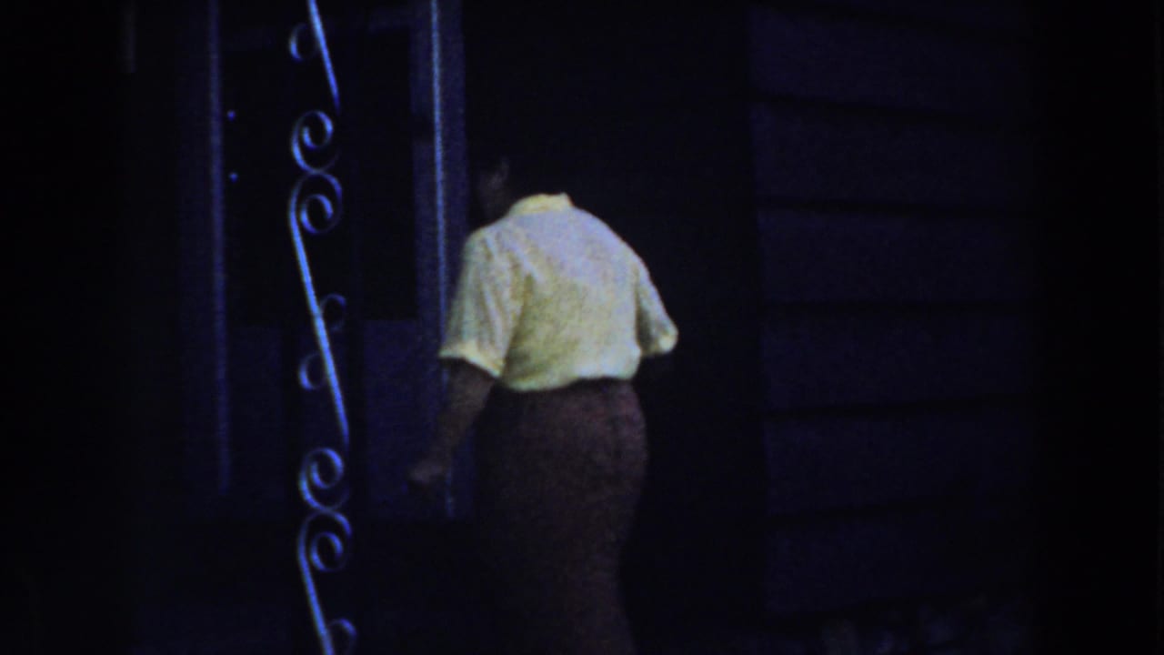 Woman nears a dark doorway with decorative metalwork beside it.