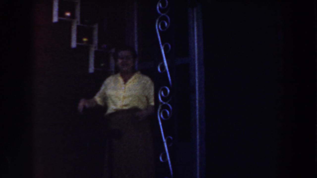 Woman in yellow shirt stands by brick wall and small white windows near a doorway.