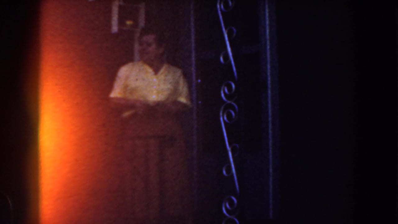 Woman in a yellow shirt standing near a doorway with decorative metalwork.