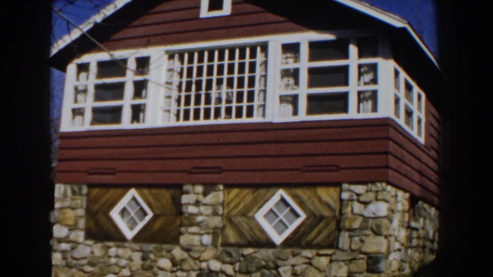 Final 1959 Michigan frame showing the cabin facade with white-trimmed upper windows, red siding, stone foundation, and decorative diamond lower windows.