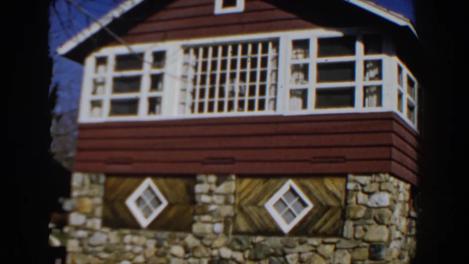 1959 Michigan 8mm frame showing a red-sided house with stone foundation, white trim, and diamond windows.