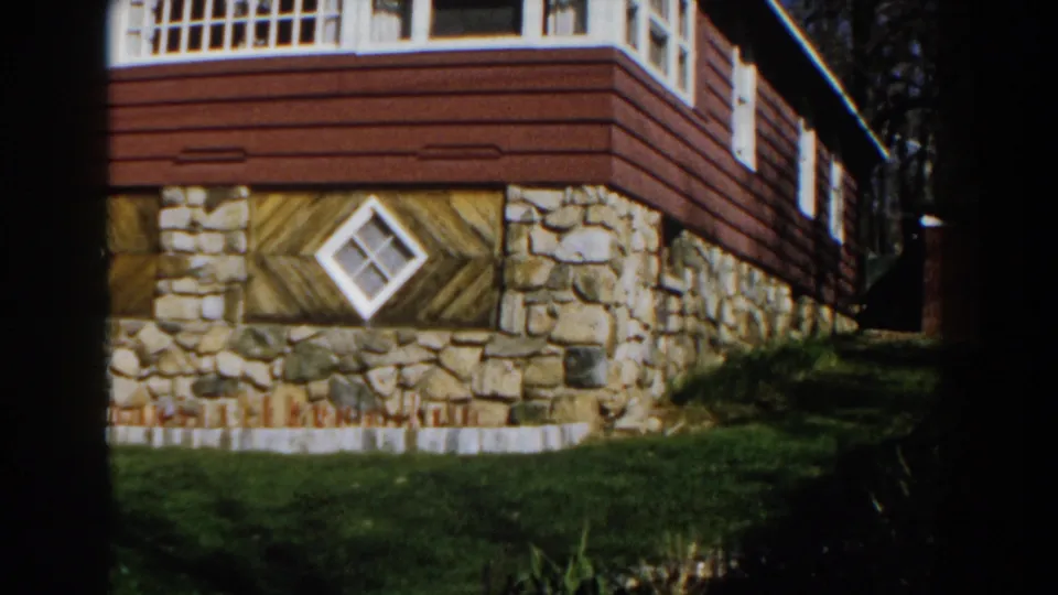 1959 Michigan 8mm frame focusing on the lower facade, stonework, grass, and a diamond-shaped white window.