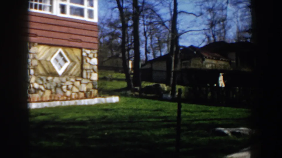 Late pan frame from the 1959 Michigan clip, showing the house edge, lawn, trees, neighboring structure, and strong shadows.