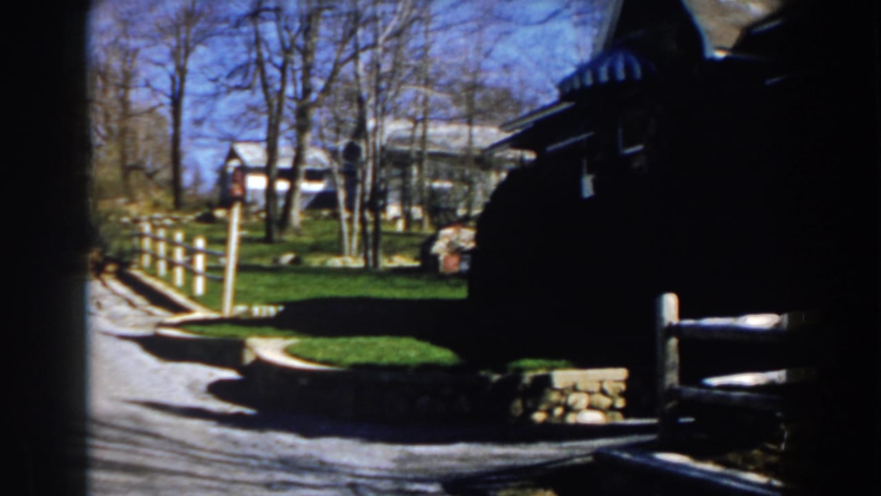 Gravel driveway beside a split-rail fence and dark house in bright sun.