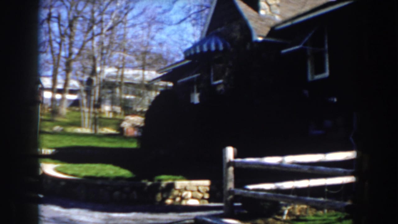 Rustic fence in front of a dark house with lawn and trees.