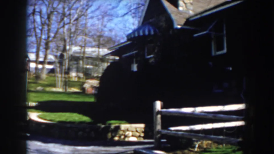 1959 Michigan frame with a rustic fence, green lawn, bare trees, and shaded wood-sided house in a country setting.