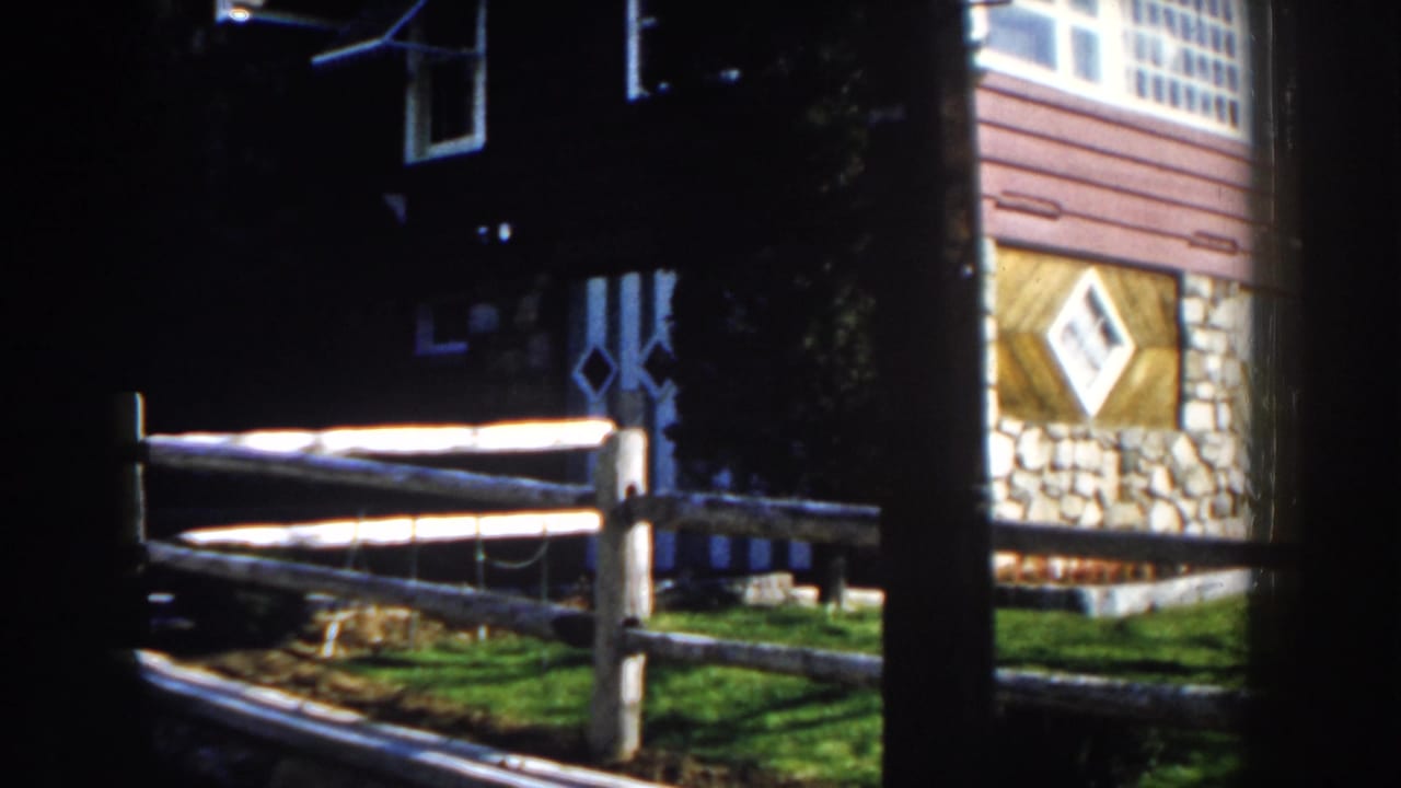 1959 Michigan 8mm frame showing a rustic cabin exterior with stone foundation, wood siding, split-rail fence, and bright lawn.