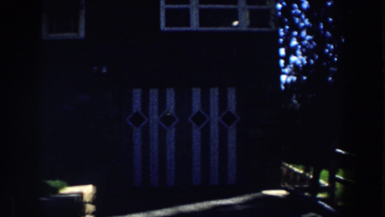 Shadowed 1959 Michigan cabin exterior with diamond-pattern panels, upper windows, and a low wooden fence rail across the foreground.