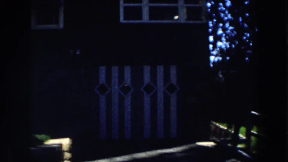 Shadowed 1959 Michigan cabin exterior with diamond-pattern panels, upper windows, and a low wooden fence rail across the foreground.