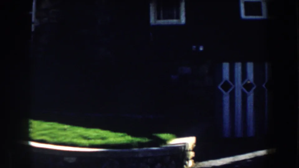 Shadowed 1959 Michigan cabin exterior with a bright patch of grass, wooden fence rail, small window, and diamond-pattern panels.