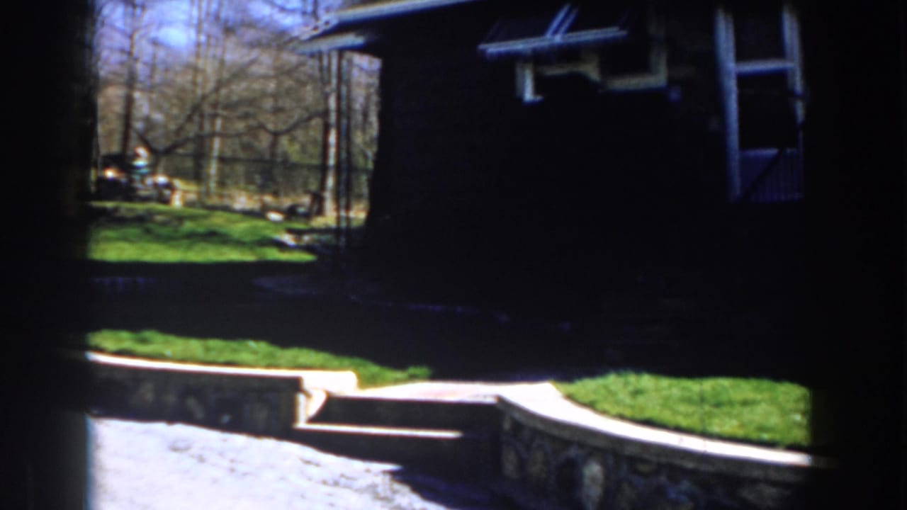 Green lawn, stone steps, retaining wall, and shadowed house beside bare trees.