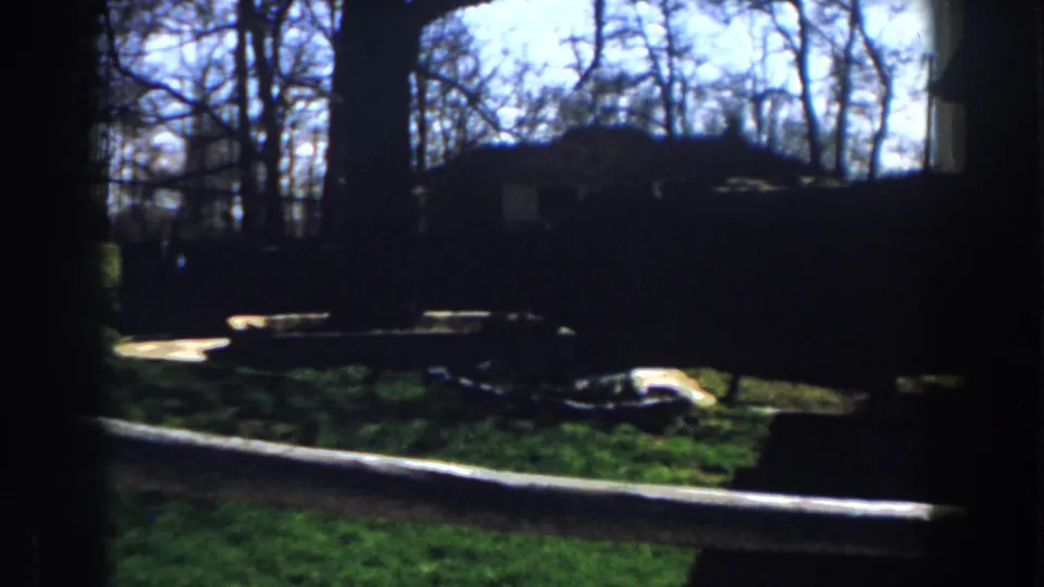 1959 Michigan 8mm view through a dark frame toward a grassy yard, bare trees, and a small outbuilding or house edge.