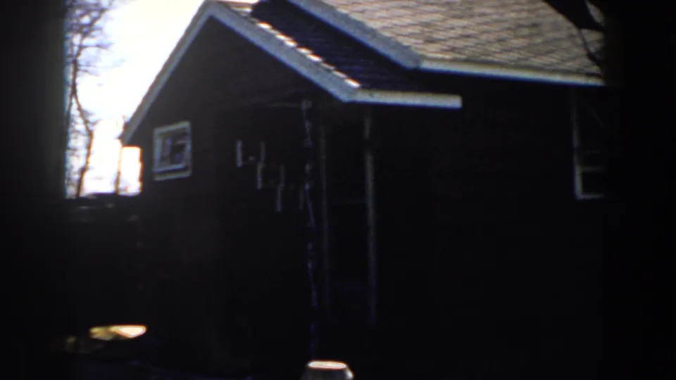 1959 Michigan 8mm frame showing a dark brown house exterior with white trim, roof eaves, and a side window.
