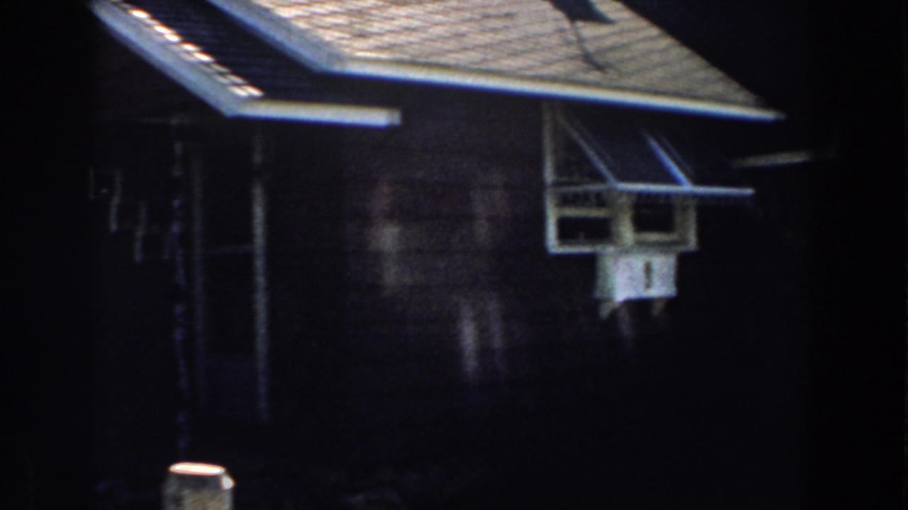 House wall with white-trimmed projecting window beneath dark roof eaves.