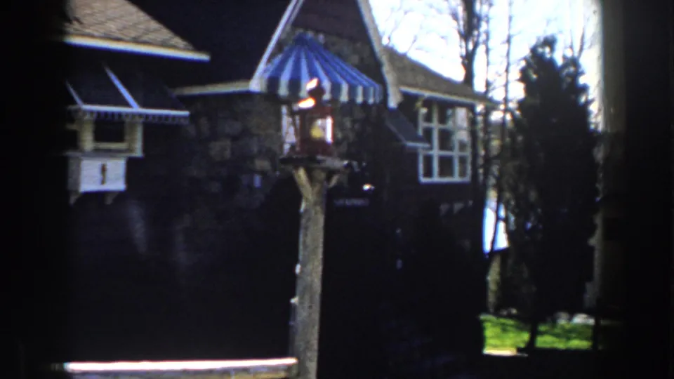 1959 Michigan home-movie frame with striped awning, yard lamp post, white-trimmed windows, bare trees, and lawn.