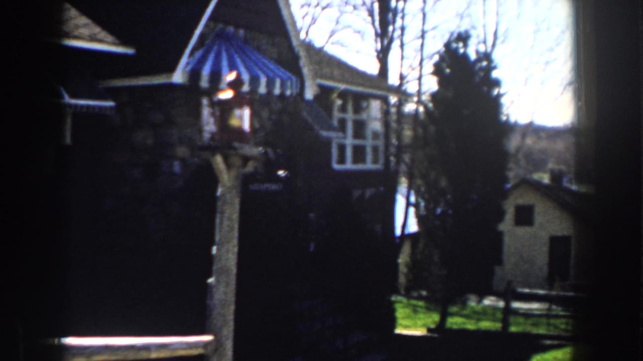 1959 Michigan 8mm frame showing a stone house, blue-and-white striped awning, lantern post, bare trees, and a small shed.