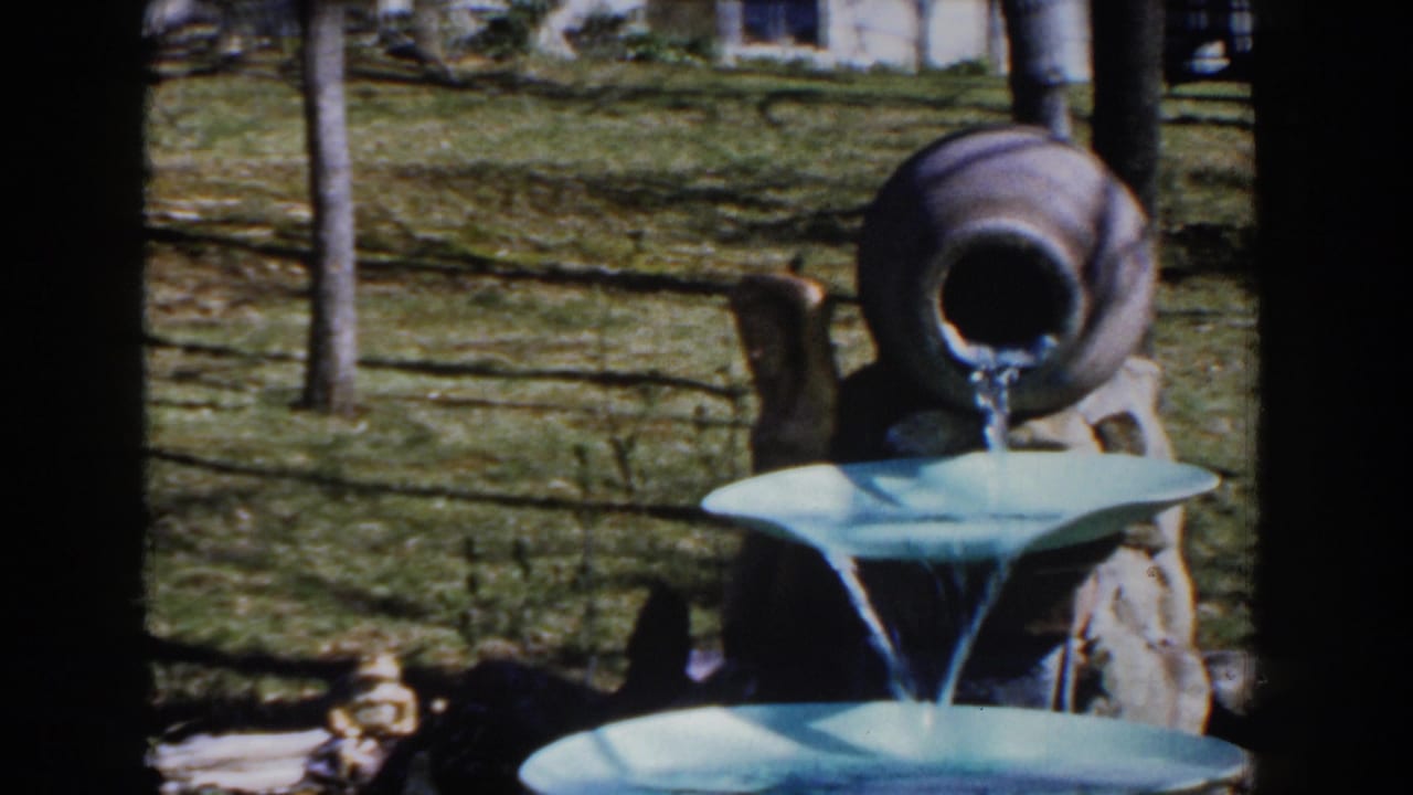 1959 Michigan 8mm frame showing a ceramic jug pouring water into a tiered light-blue garden fountain.