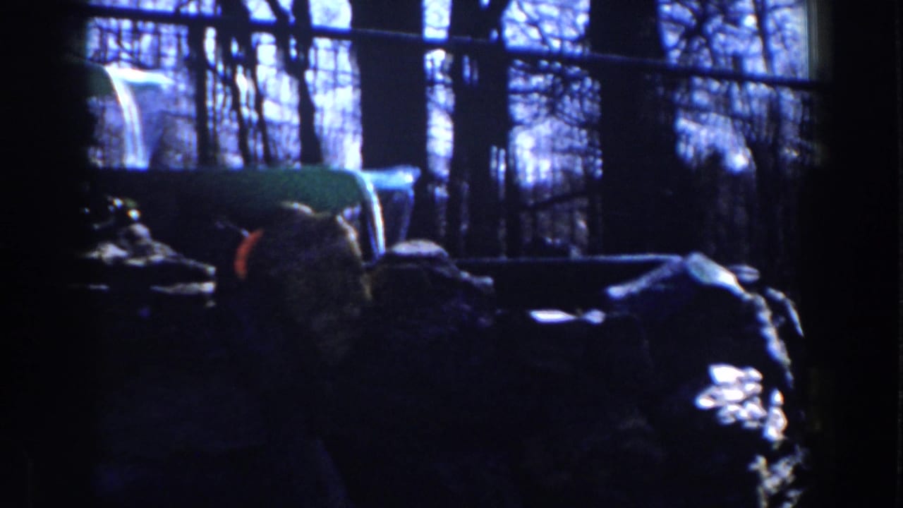 Dark view of a park fountain structure with rocks, bare trees and fence beyond.