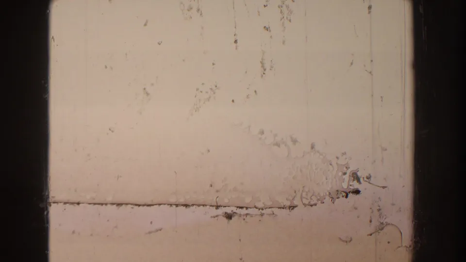Scratched and mostly blank 8mm frame from the 1959 Michigan footage, with pale exposure, dark borders, and surface debris.