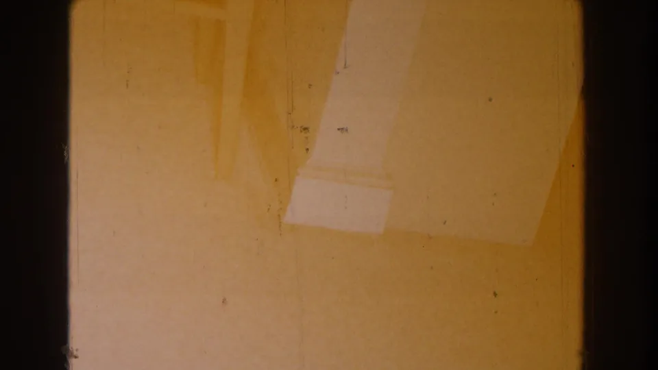 1959 Michigan home-movie frame with a pale column base, warm painted wall, dark gate edge, and scattered film dust.