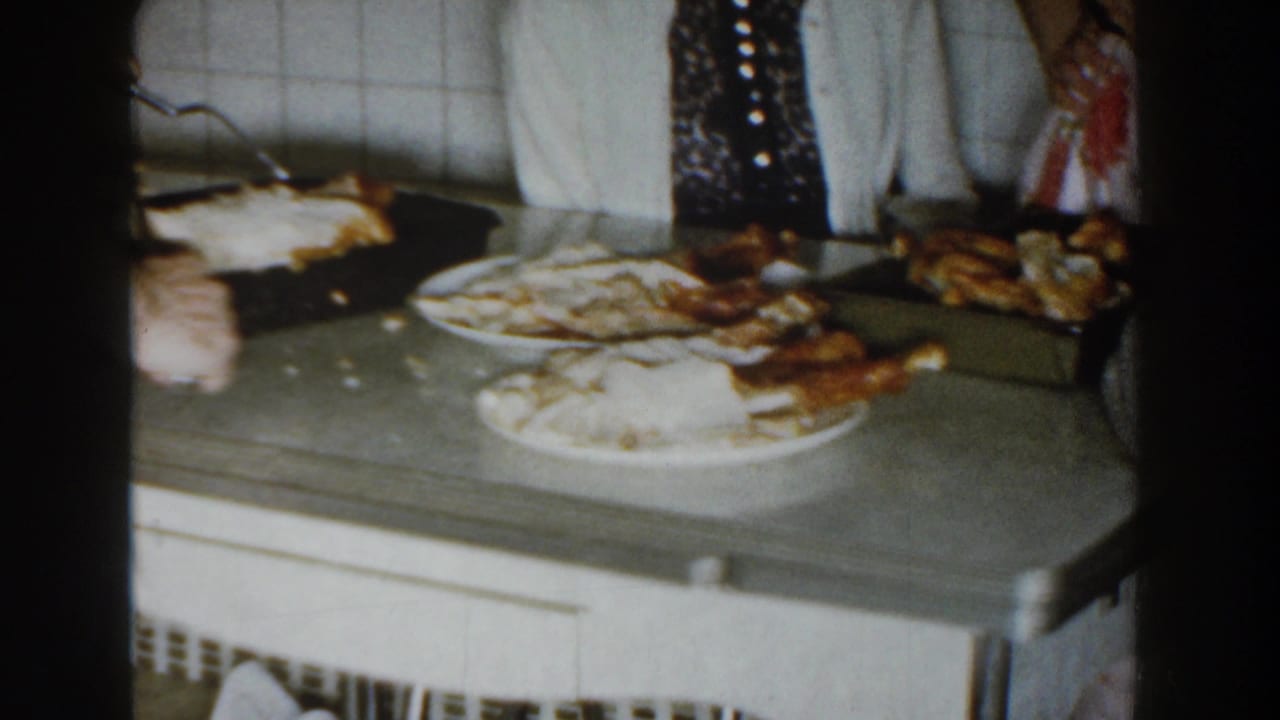Kitchen counter with plates of food, bread, and adults standing nearby.
