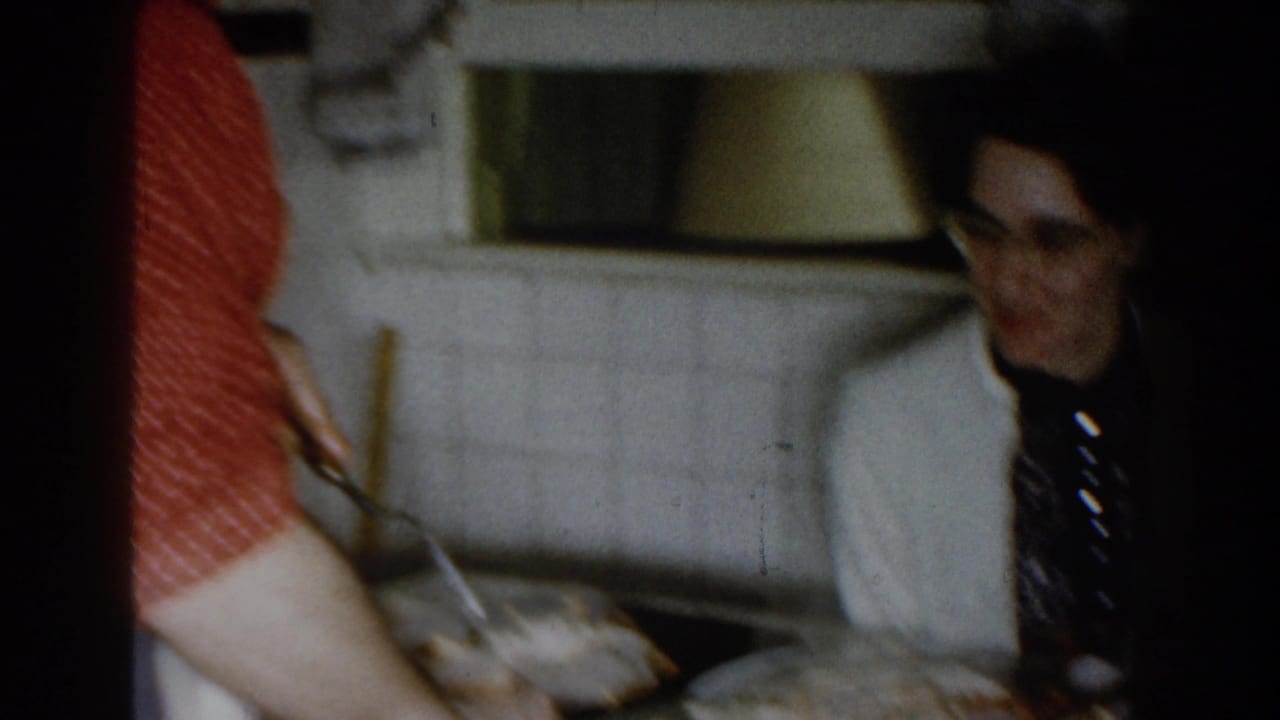 Man in a white jacket sits near a kitchen counter while food is served.