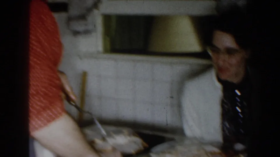 1959 Michigan kitchen scene with a man in a white jacket and patterned tie beside a counter as a person in red serves food.