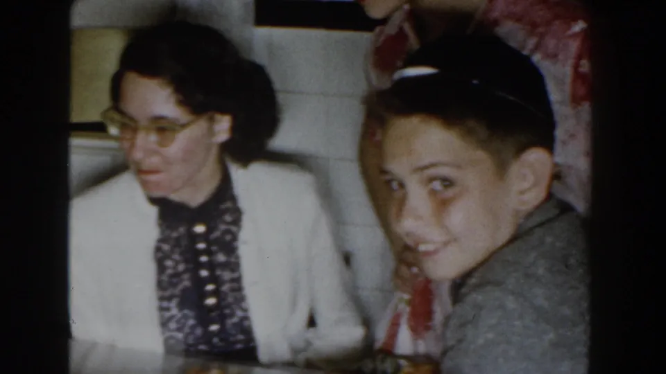 1959 Michigan home interior with a woman in glasses and a young person looking toward the camera near the kitchen serving area.