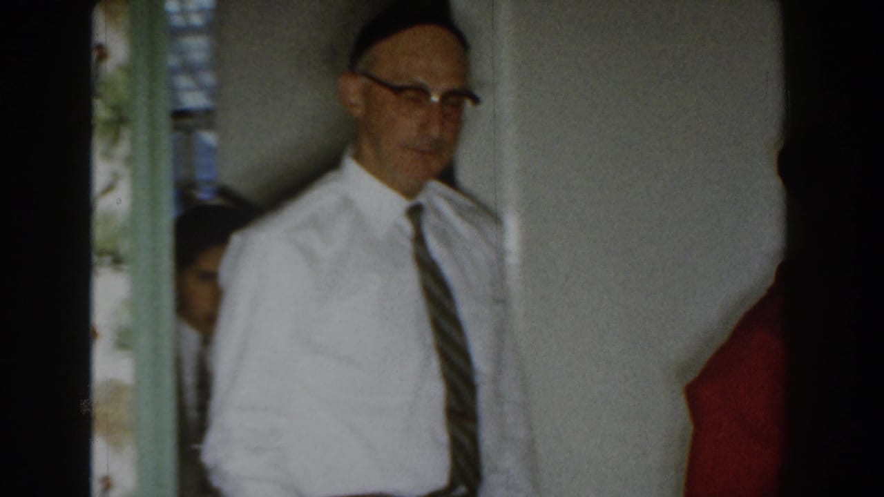 In a 1959 Michigan home interior, a man in a yarmulke, white dress shirt, and striped tie is seen near a doorway.