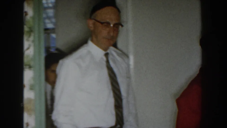 In a 1959 Michigan home interior, a man in a yarmulke, white dress shirt, and striped tie is seen near a doorway.