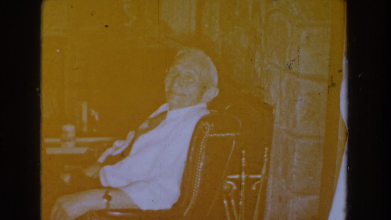 Yellow-tinted frame of the seated man in the red chair beside the fireplace.