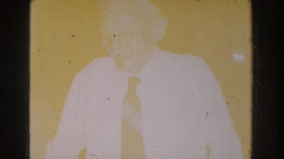 The 8mm frame becomes heavily overexposed while the elderly man in a white shirt and tie remains faintly visible.