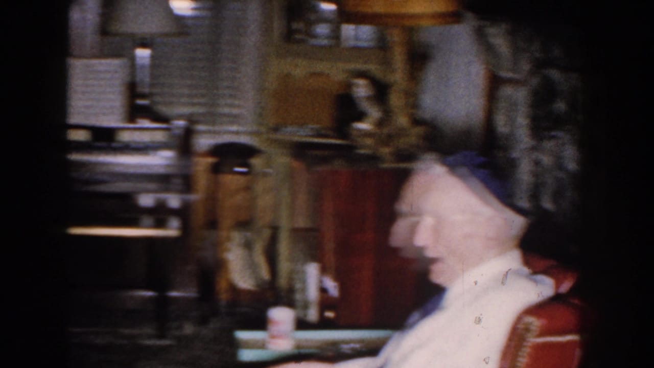 Blurred profile of an elderly man speaking from a red chair in a living room.