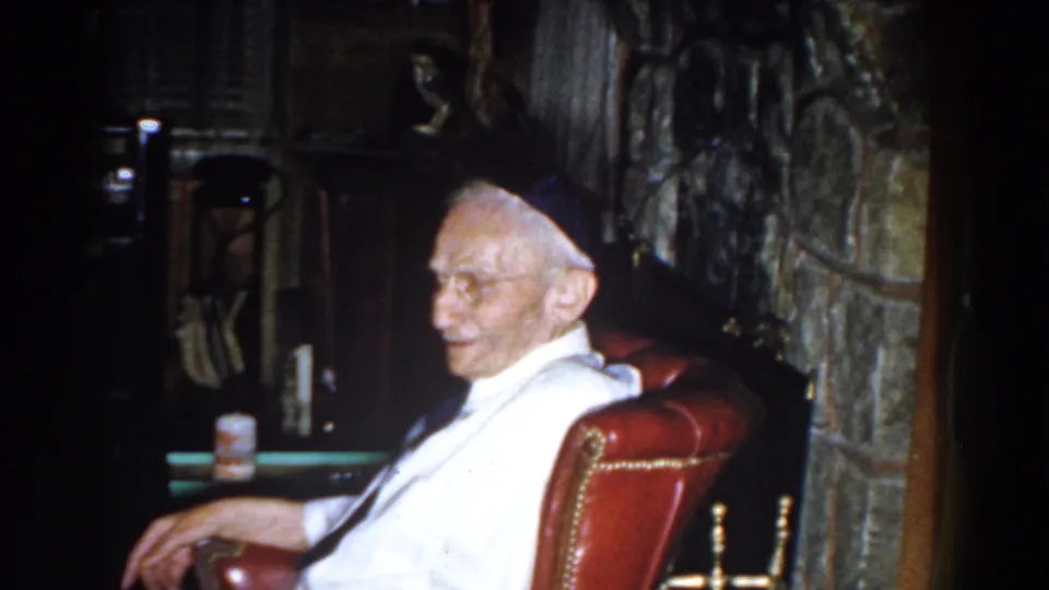 An elderly man sits in a red leather armchair near a stone fireplace inside a 1959 Michigan home.