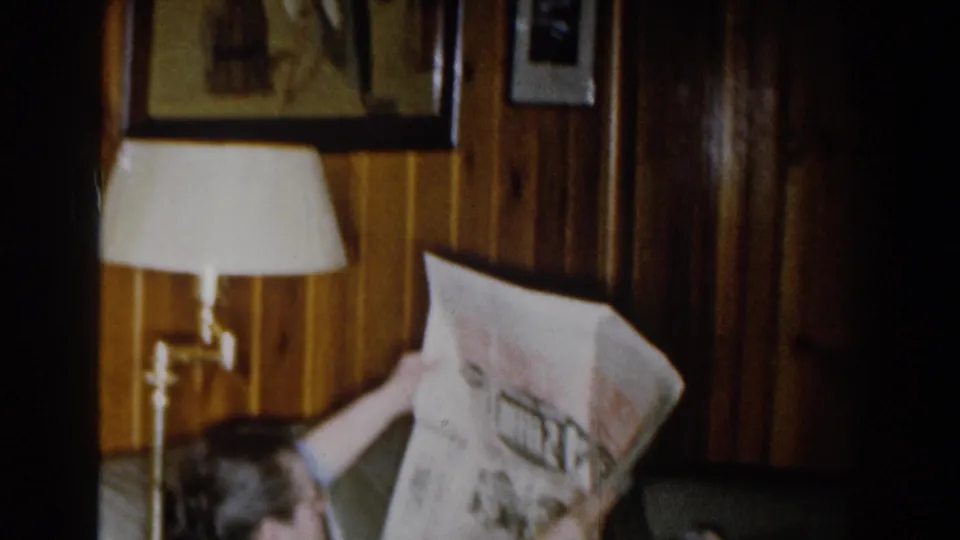 The 1959 Michigan interior shows a seated person reading a newspaper near a lamp and wood-paneled wall.