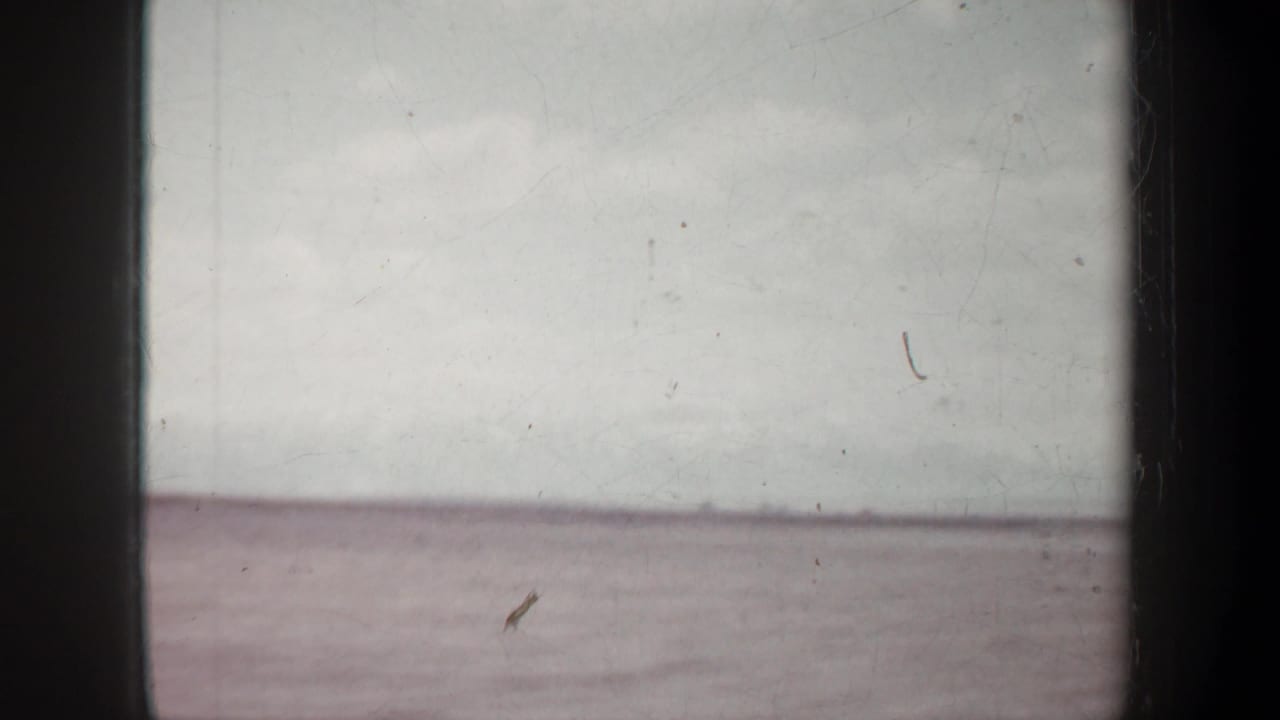 Flat distant horizon and cloudy sky seen through a scratched film frame.