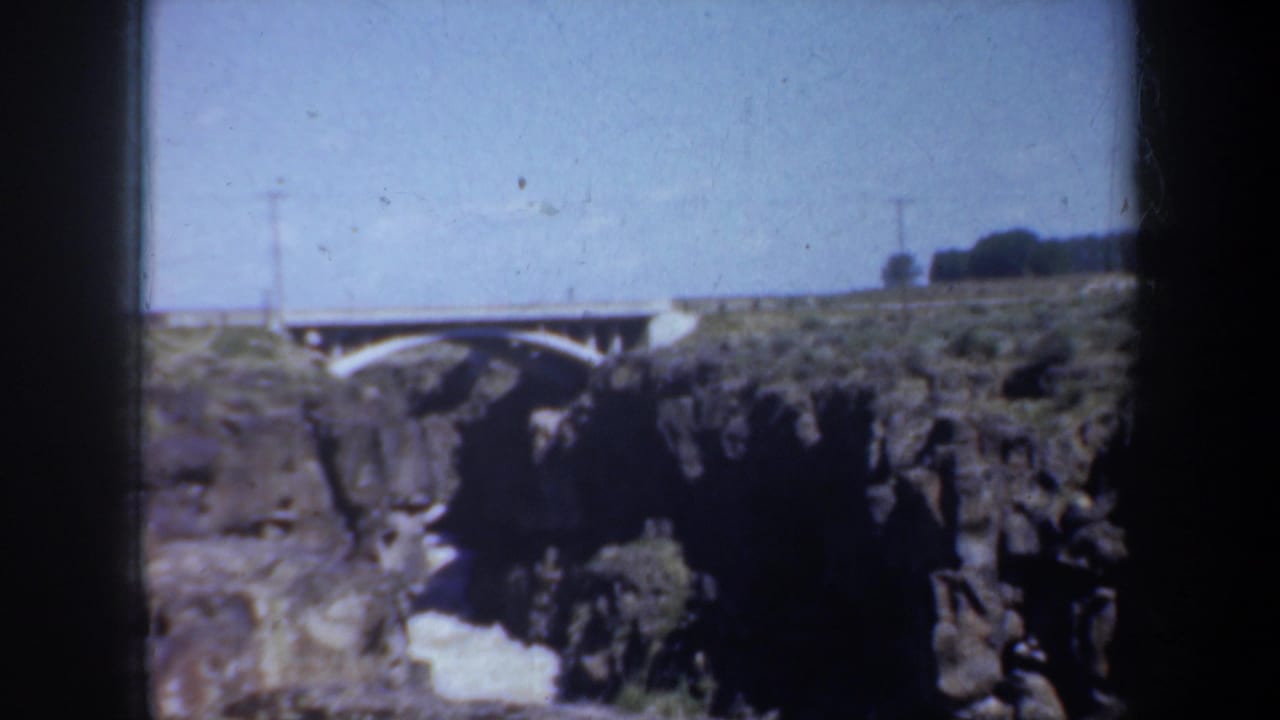 White arched bridge spanning a rocky creek canyon under a blue sky.