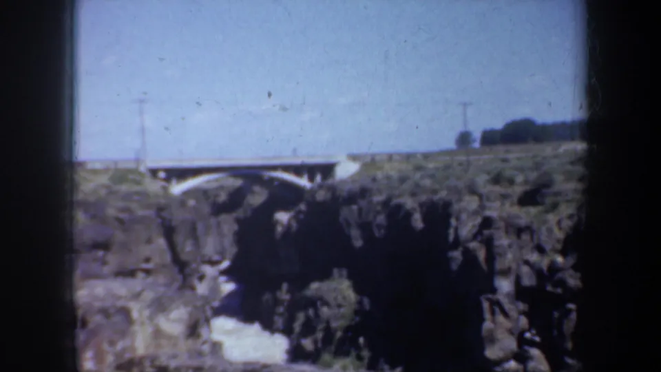 1957 Oregon 8mm frame showing a white arched bridge above a rocky creek canyon with utility poles and dark film borders.