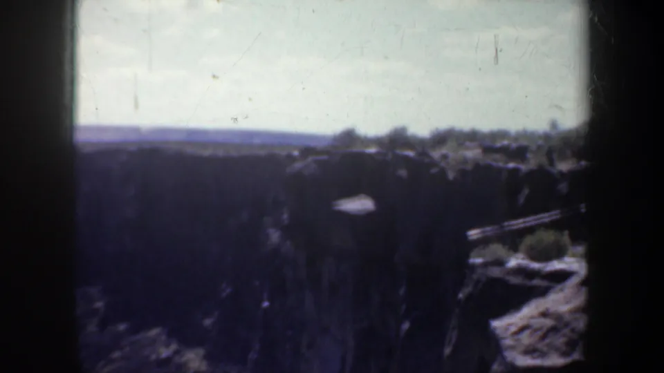 1957 Oregon 8mm view across a shadowed canyon with rocky edges, sparse vegetation, and a bright horizon.