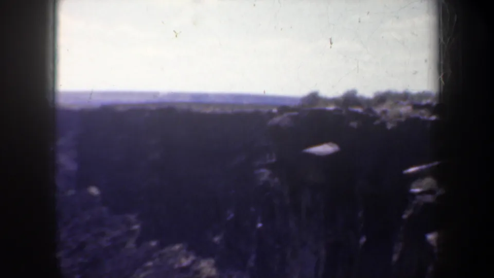 1957 Oregon home-movie frame looking over a dark canyon rim toward a pale sky and distant terrain.