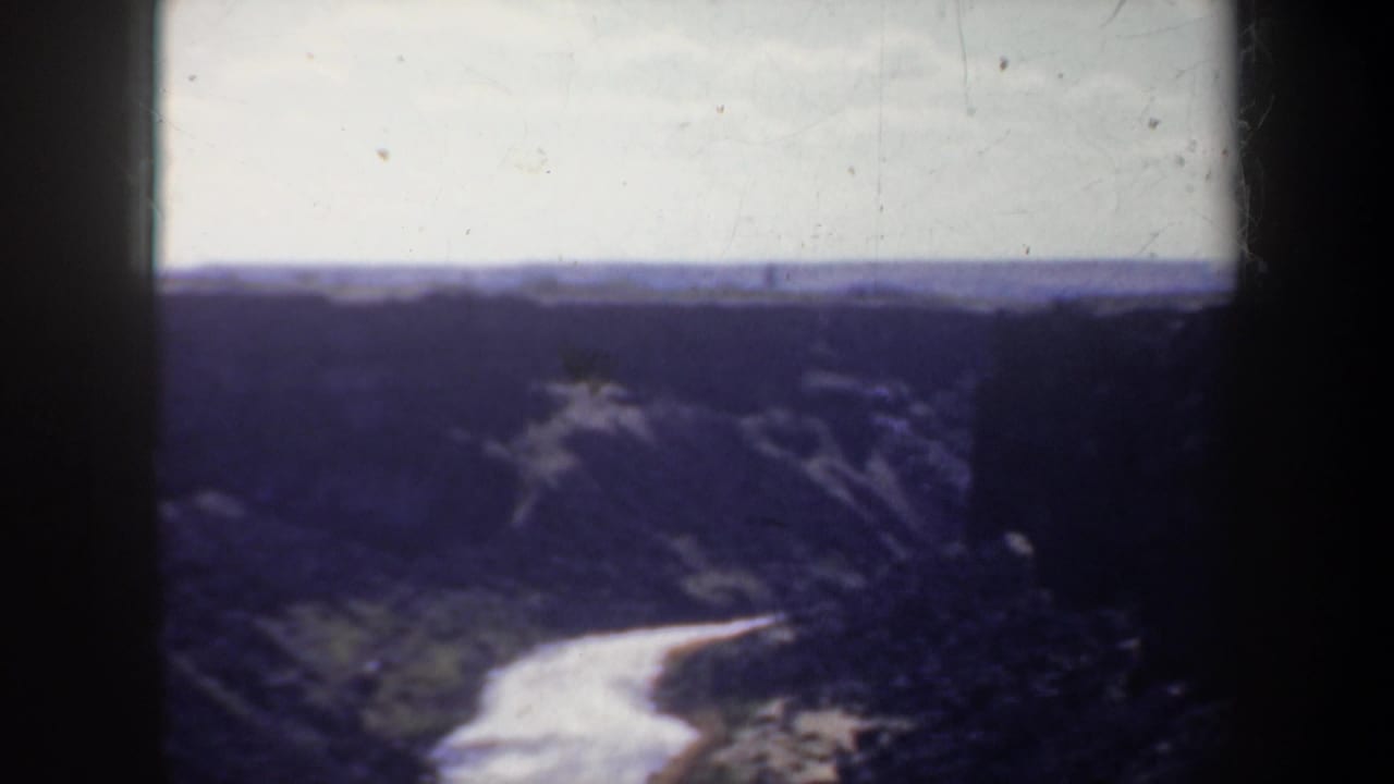 1957 Oregon 8mm home-movie frame showing a fast pale river winding through a steep, dark canyon with distant ridges and visible film-frame edges.