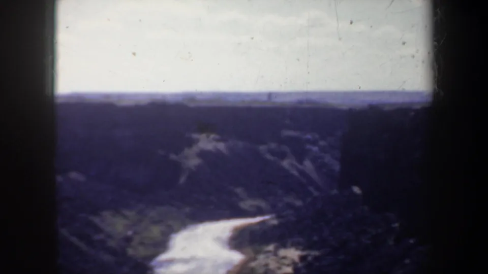 1957 Oregon 8mm home-movie frame showing a fast pale river winding through a steep, dark canyon with distant ridges and visible film-frame edges.