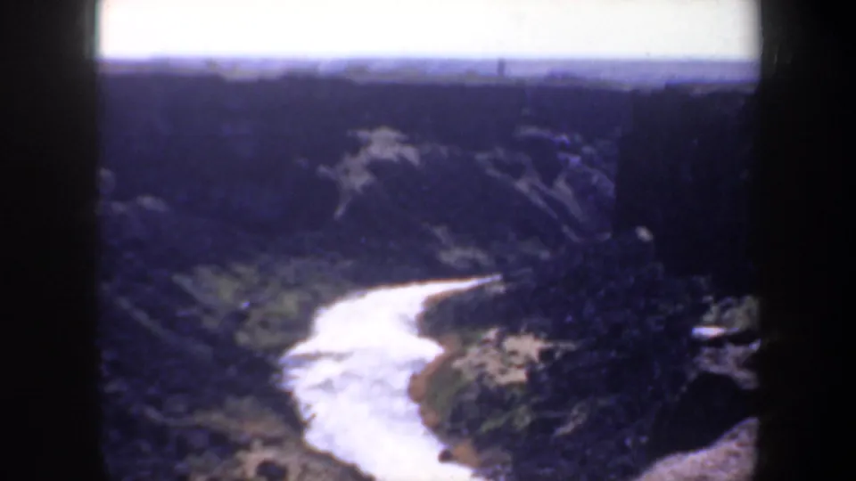 1957 Oregon 8mm frame showing the river receding through a deep canyon, with distant dark mountains, pale sky, and soft archival film texture.