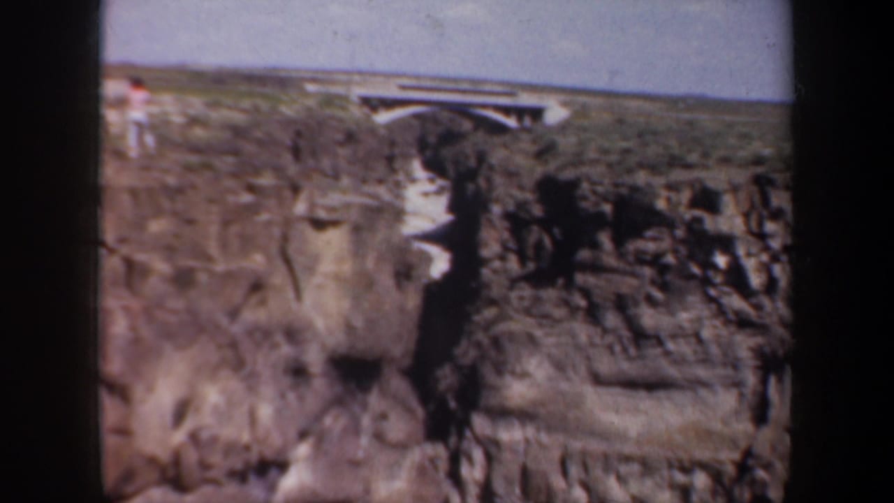 Rocky canyon wall with a bridge visible near the horizon above the gorge.