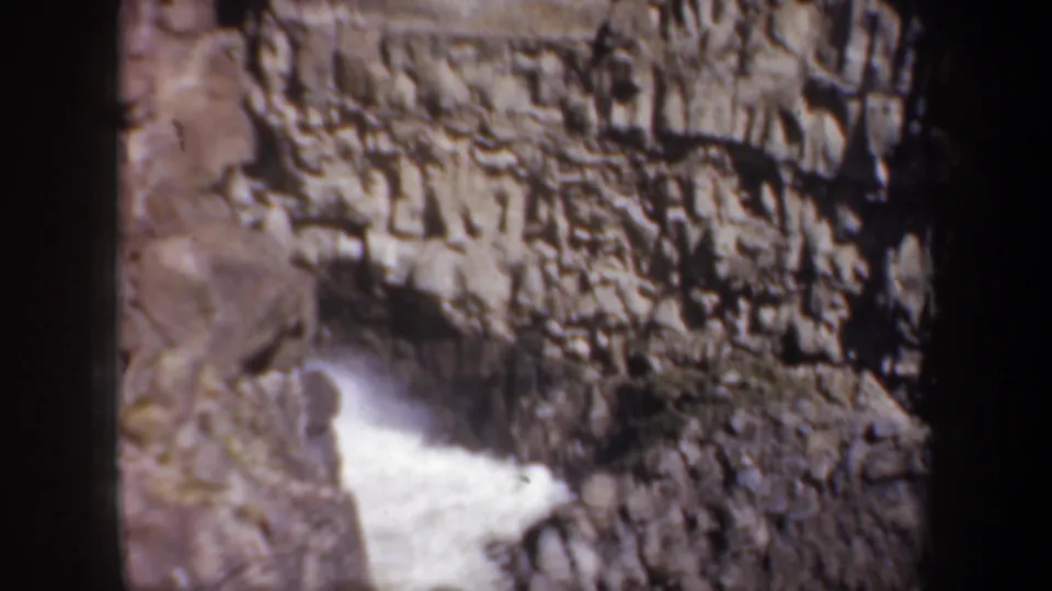1957 Oregon canyon frame showing steep eroded rock and bright white water at the bottom of the gorge.