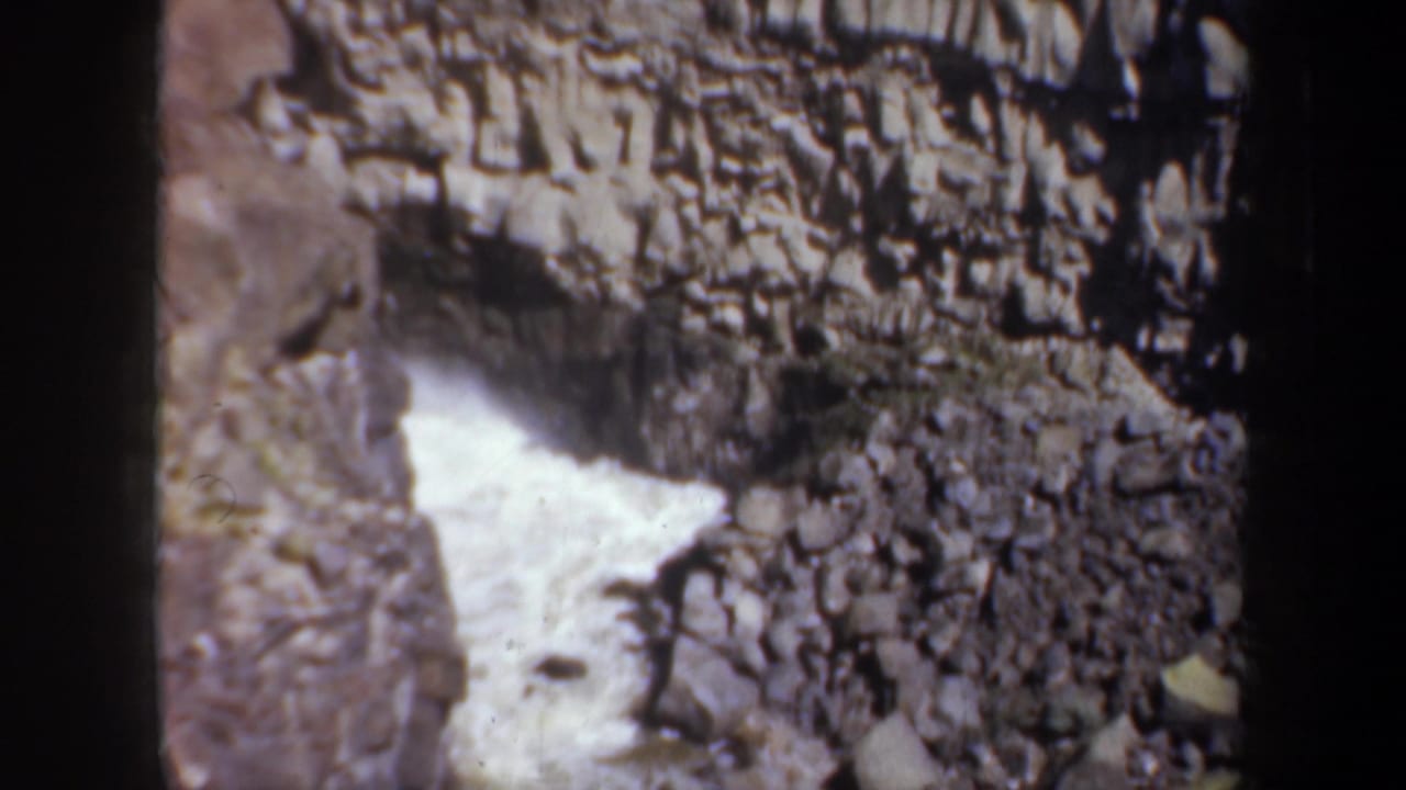 1957 Oregon 8mm frame showing turbulent river water cutting through grey rock formations in a steep canyon.