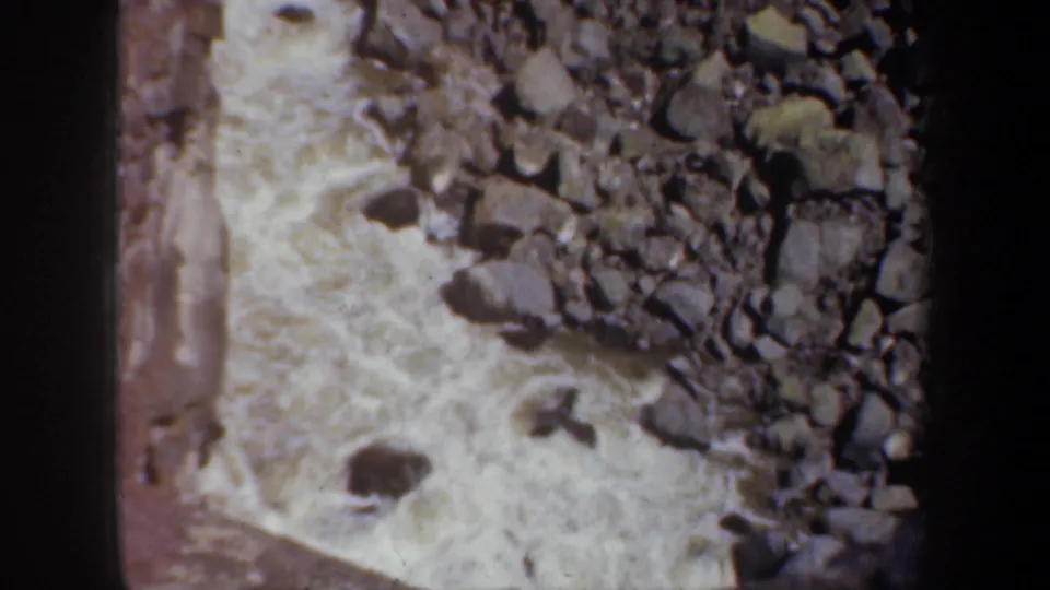 1957 Oregon 8mm frame looking down on pale rapids, large rocks, and a steep canyon edge.