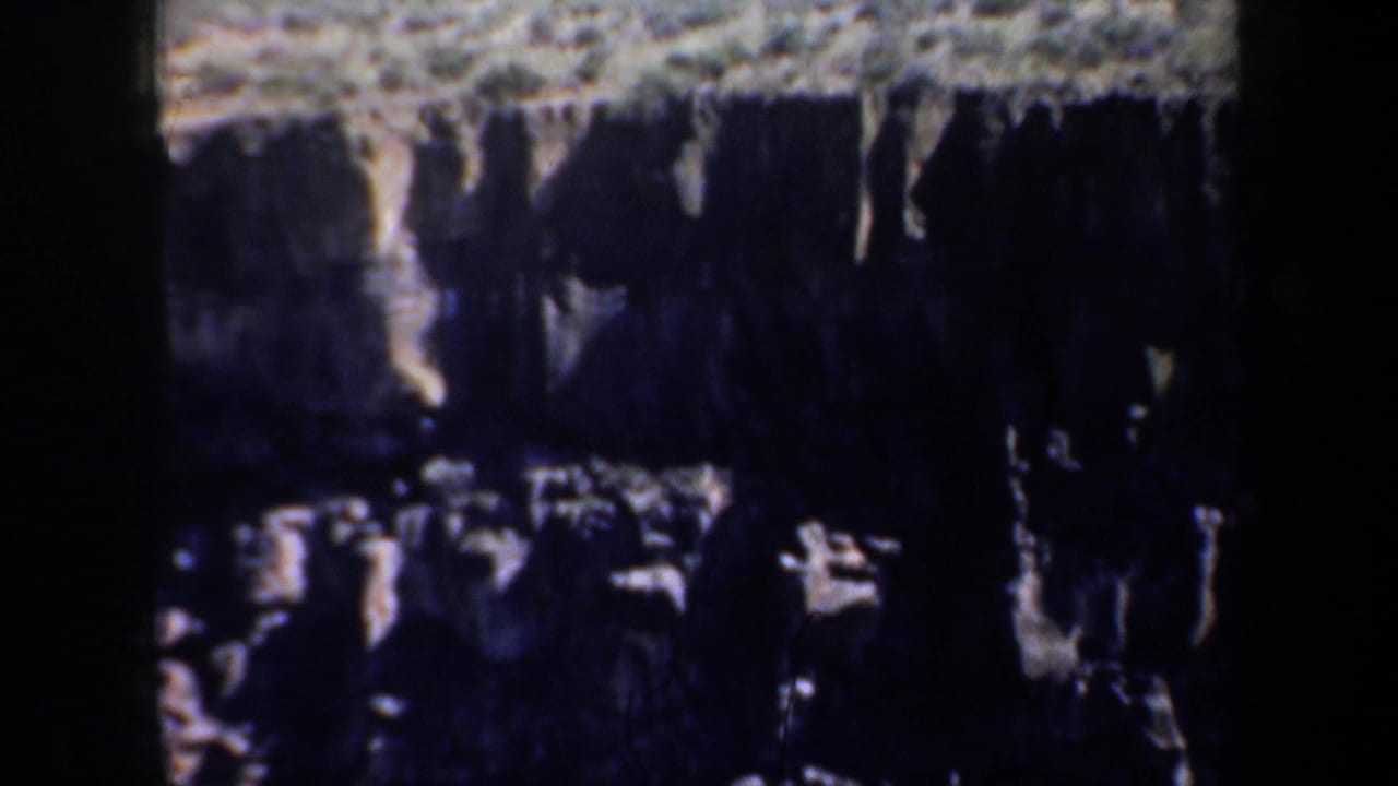 1957 Oregon 8mm frame showing a rugged cliff face with layered stone, pale ledges, and heavy shadow across the rock wall.
