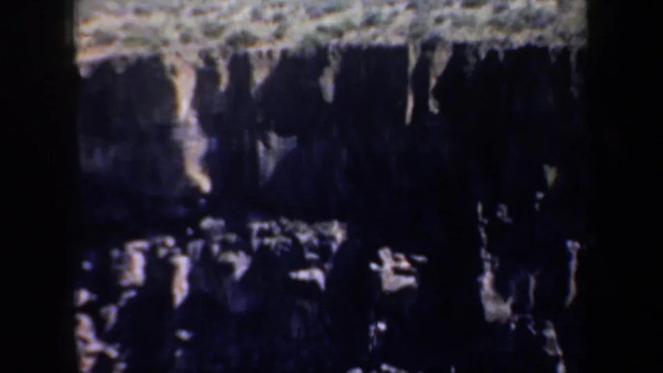 1957 Oregon 8mm frame showing a rugged cliff face with layered stone, pale ledges, and heavy shadow across the rock wall.