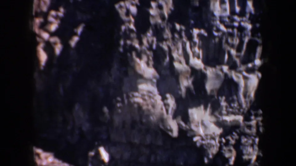 1957 Oregon 8mm frame showing a closer view of rough cliff textures, pale outcrops, and shadowed recesses in the rock.